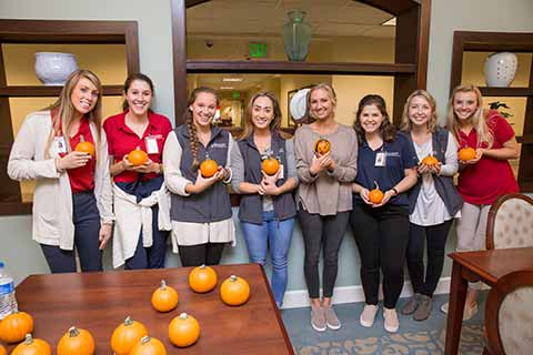 eight female students holding small decorated pumpkins
