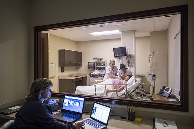 A faculty member observes two nursing students in a high-fidelity simulation room
