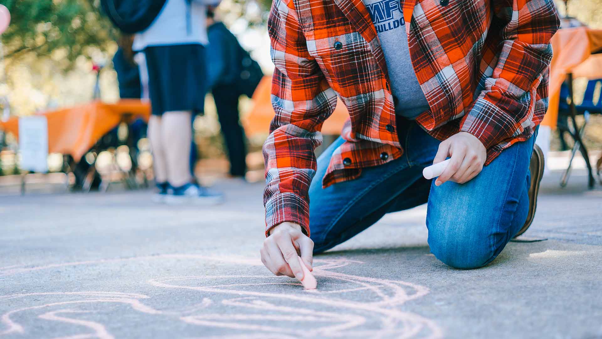 male student drawing on sidewalk with chalk