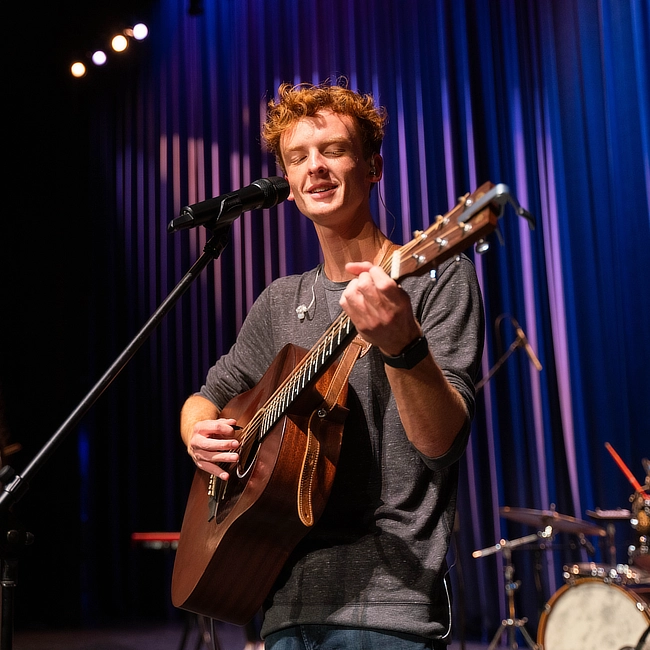 male student playing guitar for worship